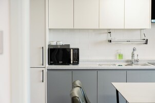Una cocina moderna con armarios blancos, un microondas negro y un lavamanos de acero inoxidable.