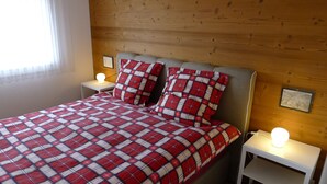 A bedroom with a plaid bedspread, two bedside lamps, and a wooden headboard. - Elfe Apartments Studio for 2 Adults, Balcony With Lake and Mountain View (Emmetten)