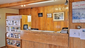 A wooden reception desk with a computer, a bulletin board with flyers, and a framed picture on the wall. - Rodeway Inn Cody (Cody)