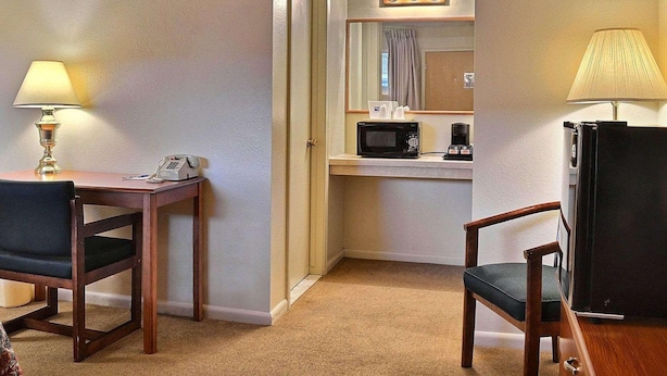 A hotel room with a desk, two chairs, a microwave, a coffee maker, and a refrigerator. - Rodeway Inn Cody (Cody)