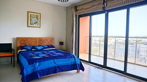 A bedroom with a large bed, a chair, a nightstand, a window with a view, and a framed picture on the wall.