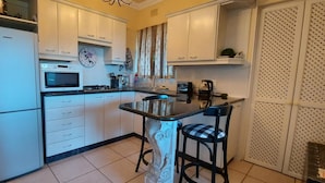 A compact kitchen with white cabinets, a microwave, a gas stove, and a small island with two stools. - Room in Apartment - The Garden Apartment - Roosboom Luxury Facilities in Somerset West, 2 Guests (Cape Town)