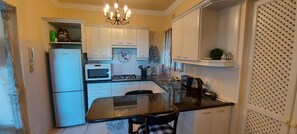 A compact kitchen with white cabinets, a black countertop, a chandelier, and a clock on the wall.