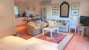 Ein gut beleuchtetes Wohnzimmer mit einer Couch, einem Couchtisch und einem Fernseher. Im Hintergrund ist eine Küchenzeile mit Schränken und einem Fenster zu sehen.