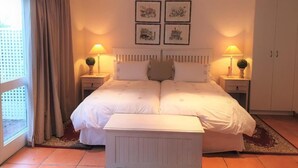 Ein ordentlich eingerichtetes Schlafzimmer mit einem großen Bett, zwei Nachttischen mit Lampen, einem weißen Kleiderschrank und einem Fenster mit Vorhängen.