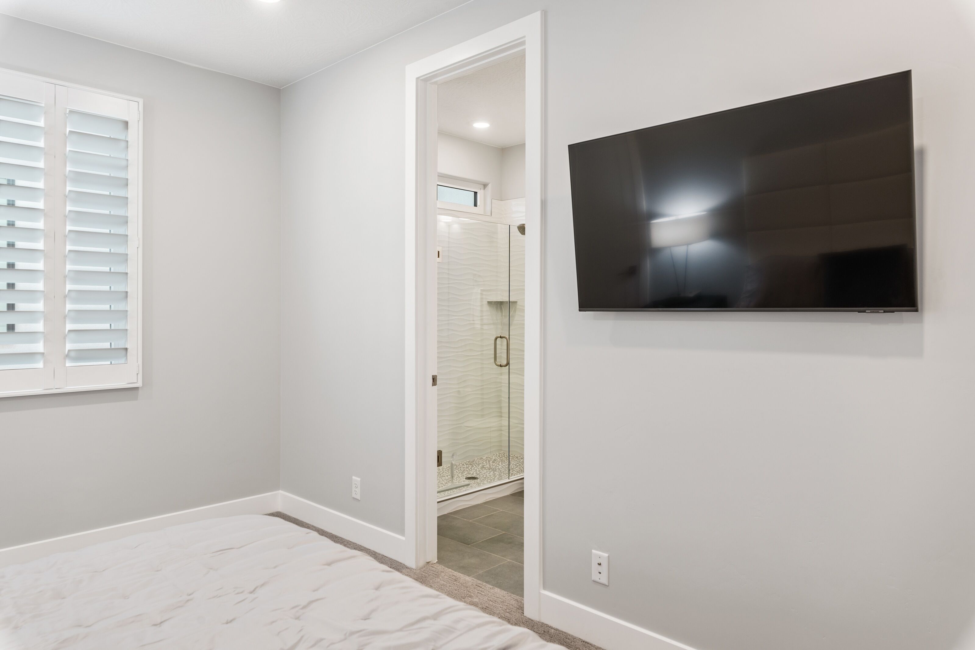 A room with a large flat-screen TV mounted on the wall, a walk-in closet, and a glass shower enclosure.