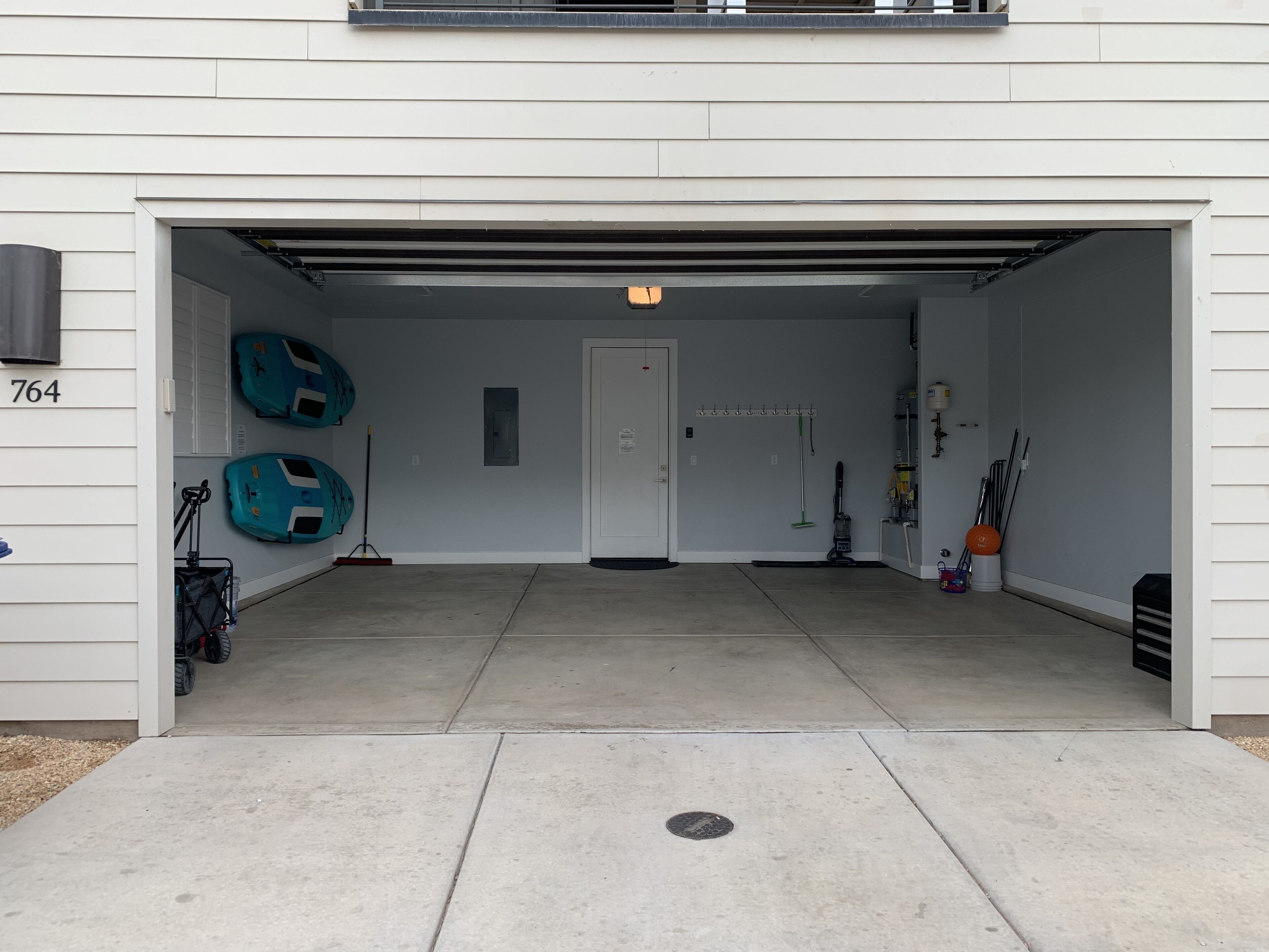 Ett garage med en vit dörr, två blå kajaker, en sopborste, en dammsugare och en vattenpump.