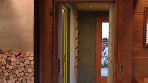 A wooden hallway with a stack of firewood on the left, a green door, and a view into another room. - Appartement for Holiday Lodge 1891 (Stalden)