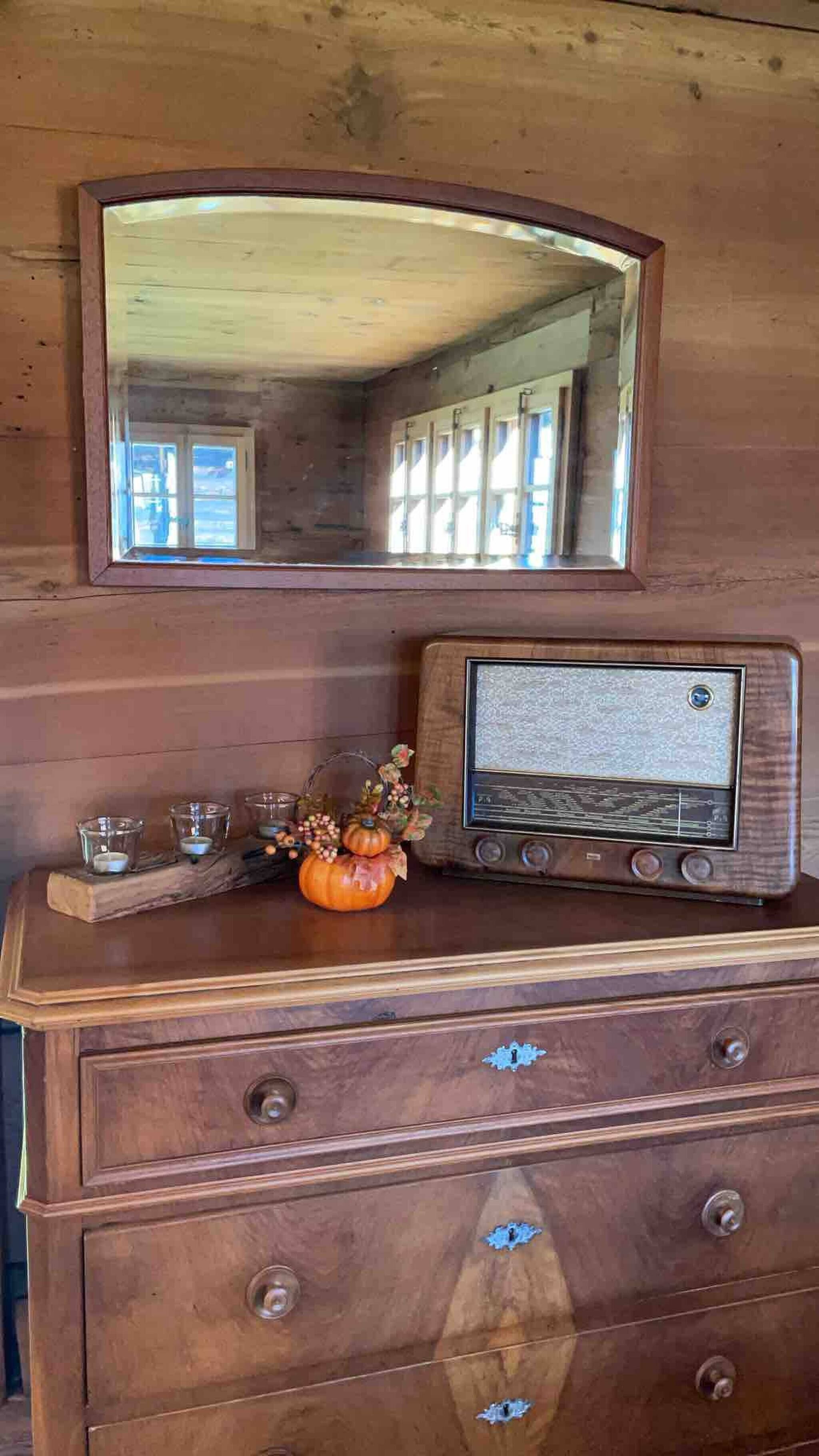 Un armari de fusta amb un aparell de ràdio, un mirall i una carbassa decorativa.