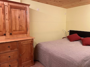 A bedroom with a wooden cabinet, a bed with red pillows, and a plain wall. - Appartement for Holiday Lodge 1891 (Stalden)