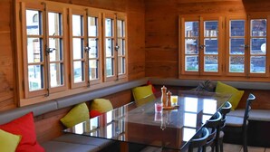 A wooden cabin interior with a glass-top dining table, wooden benches, and large windows. - Appartement for Holiday Lodge 1891 (Stalden)
