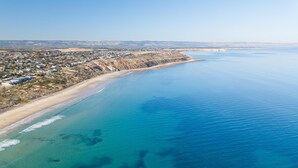 Une vue aérienne d’une ville côtière, avec une plage, des eaux d’un bleu limpide et un phare situé au loin.
