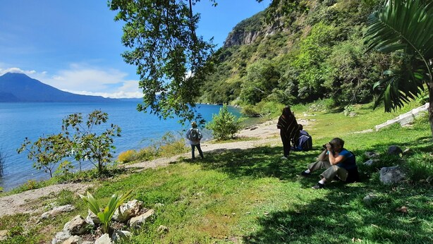 A coastal area with a mountain in the background, grassy terrain, and a body of water. - Casa Buen Aventura, Panajachel, Solola, Guatemala - Casa de Campo Familiar (Sololá)