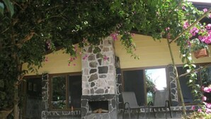 A stone fireplace with a stone surround, a covered patio area with chairs, and a view of a building with large windows. - Casa Buen Aventura, Panajachel, Solola, Guatemala - Casa de Campo Familiar (Sololá)