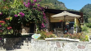 A stone-walled outdoor seating area with a table and chairs, surrounded by vibrant bougainvillea flowers. - Casa Buen Aventura, Panajachel, Solola, Guatemala - Casa de Campo Familiar (Sololá)
