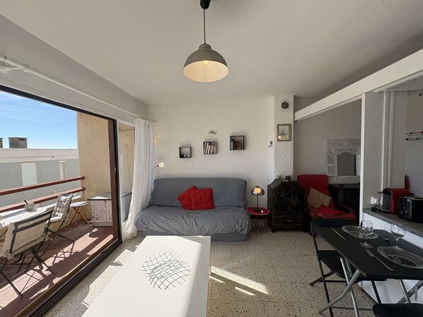 Un espace de vie compact doté d’un balcon, d’un canapé, d’une table à manger pour deux personnes et d’une kitchenette.