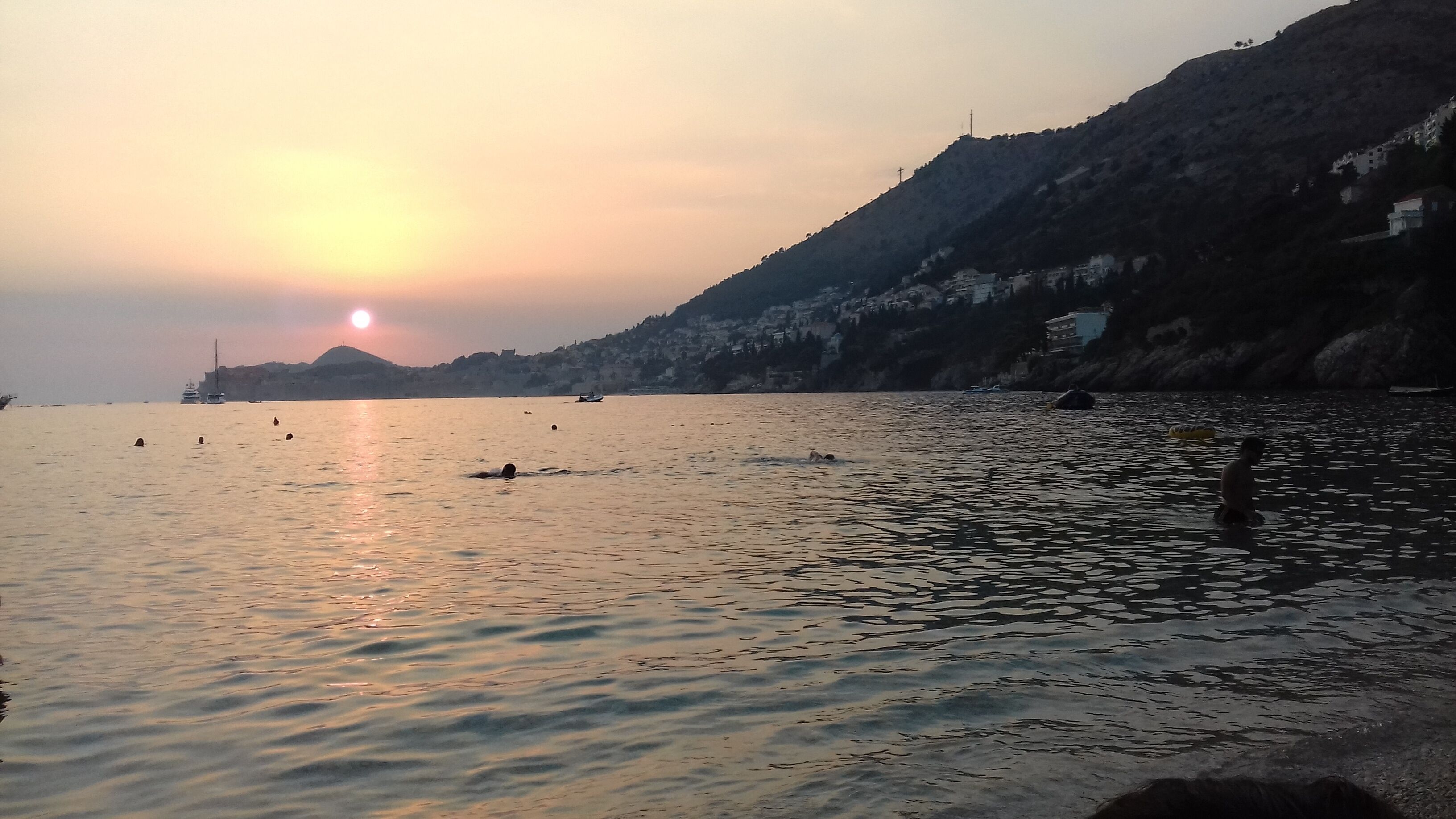 Ruhiges Gewässer mit Booten, einem Sonnenuntergang und einer hügeligen Landschaft.