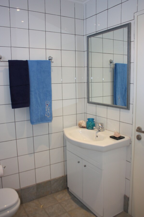 A bathroom with white tiles, a sink, a mirror, and two towels.