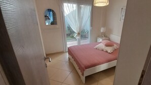 Een slaapkamer met een bed, nachtkastje, lamp en raam met uitzicht op groen.