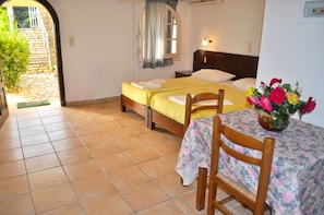 Two single beds with made bedsheets and pillows, a bedside table, and a floral-patterned table with chair.