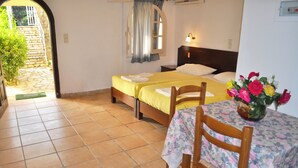 A room with two beds, a table with a floral tablecloth, and a vase of flowers. - Studio Apartments Maria With Pool and Amazing View - Agios Gordios Beach (Corfu)