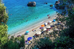 Una playa con agua turquesa cristalina, gente nadando y sombrillas en la arena.