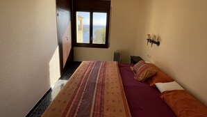 A bedroom with a bed, a window with a view of the sea, a radiator, and a wall-mounted lamp. - "Roc del amor" Villa first line sea pool (Roses)