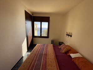 Quarto com cama, janela vista para o mar, radiador e luminária na parede.