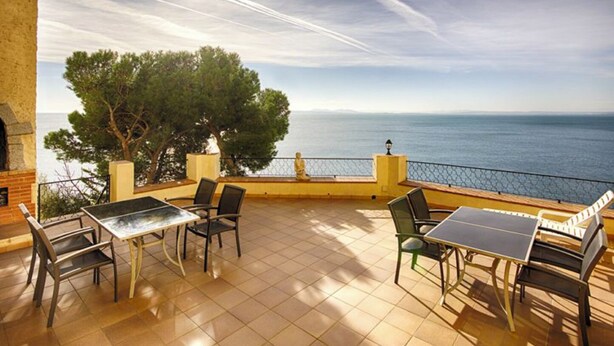 A terrace with a view of the sea, featuring a table and chairs, a tree, and a railing. - "Roc del amor" Villa first line sea pool (Roses)