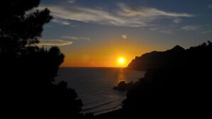 Un atardecer sobre un paisaje costero con afloramientos rocosos y siluetas de árboles.