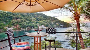 A terrace with a table and chairs, overlooking a body of water and a hillside.