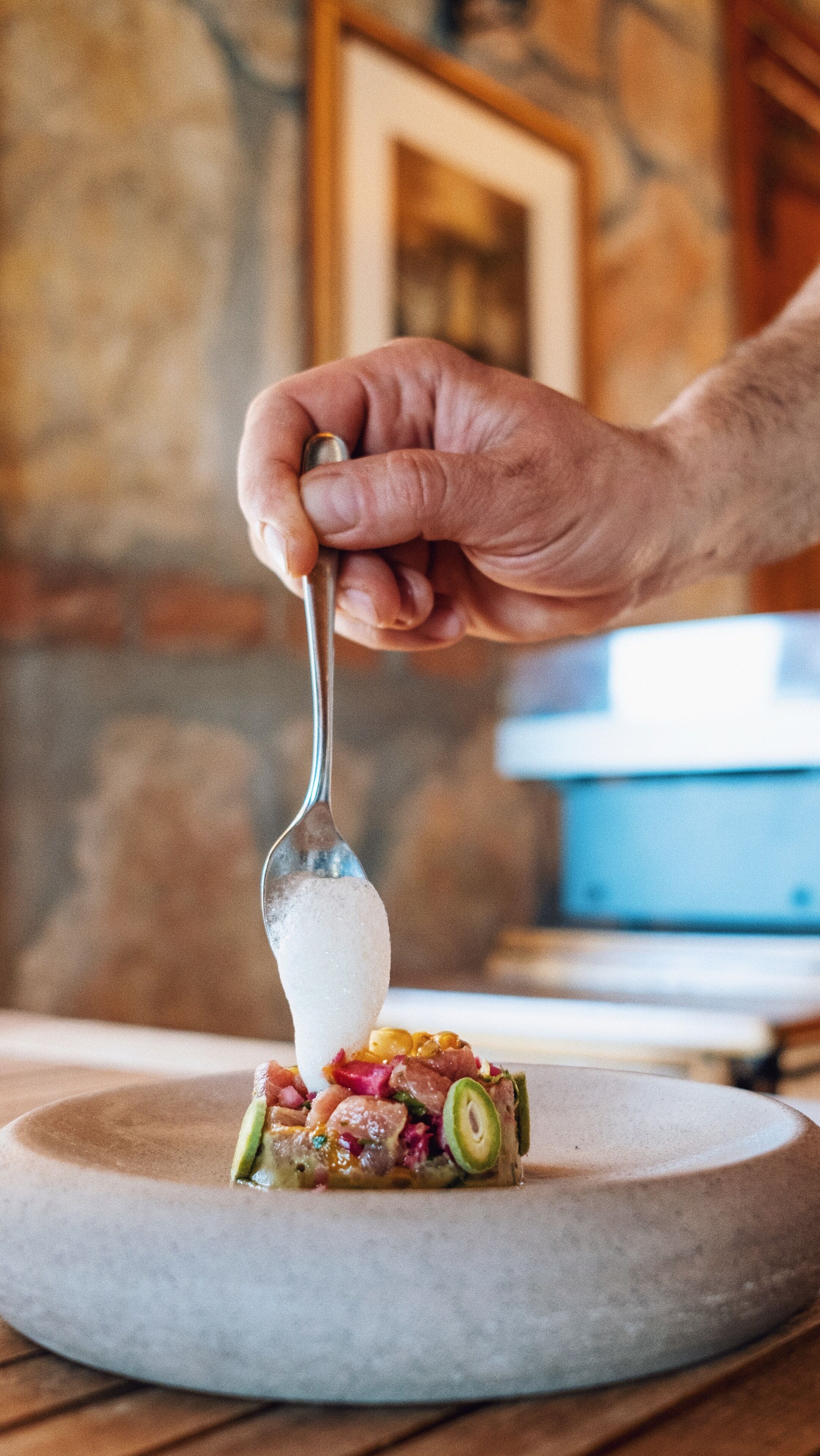 A hand holding a spoon over a dish with various ingredients.