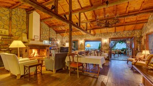 A rustic interior with a stone fireplace, wooden ceiling beams, and a dining area with a view of the outdoors. - Olympos Mountain Lodge (Kemer)