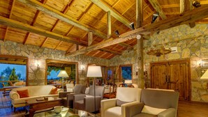 A spacious living area with a stone wall, wooden ceiling beams, and comfortable seating. - Olympos Mountain Lodge (Kemer)