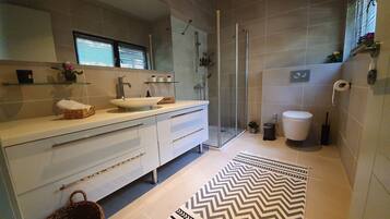 Un baño moderno con cabina de ducha de vidrio, un lavabo blanco y un espejo grande.