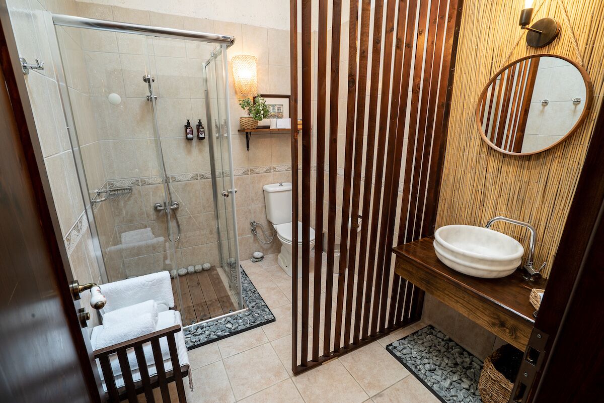 A modern bathroom with a glass-enclosed shower, a wooden vanity with a round sink, and a vertical wooden panel.