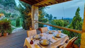An outdoor dining area with a wooden deck, stone pillar, and table set for a meal. - Olympos Mountain Lodge (Kemer)