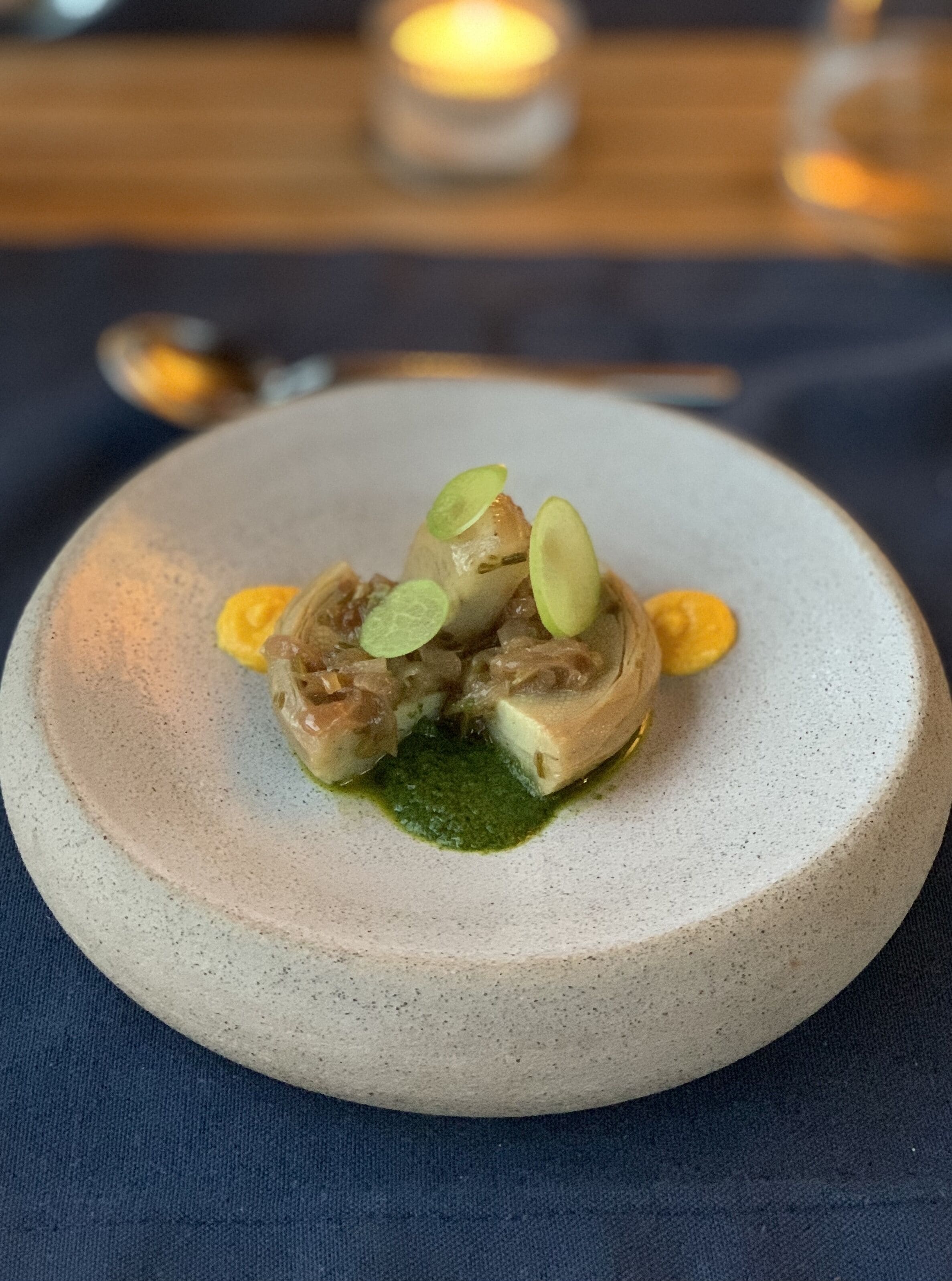 A plate with a dish of meat and green garnish on a speckled ceramic plate.
