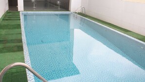 A rectangular swimming pool with a tiled edge, a metal ladder, and a grassy area beside it. - Room-royalrex Hotel-guest Suite (Lagos)