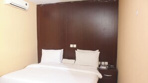A hotel room with a large bed, a wooden headboard, a bedside table with a phone, and an air conditioning unit on the wall. - Room-royalrex Hotel-guest Suite (Lagos)