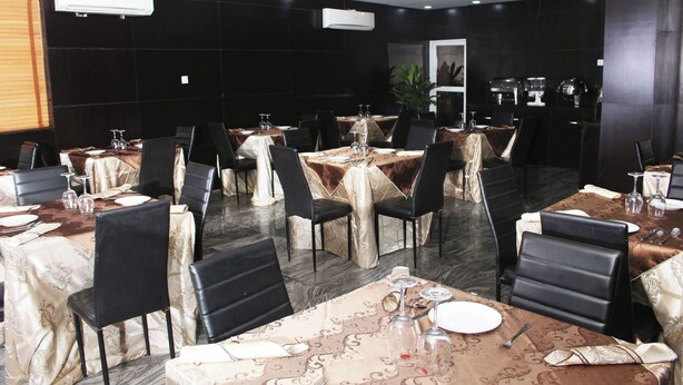 A dining area with tables set for multiple guests, featuring black chairs and tables covered with patterned tablecloths. - Room-royalrex Hotel-guest Suite (Lagos)