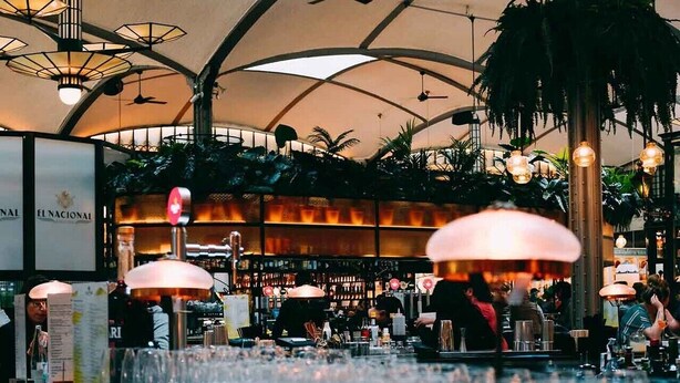 A bar area with a high ceiling and multiple hanging lights. There are numerous empty glasses on the counter, and a sign for 'El Nacional' is visible in the background. - Room-aerol Hotel and Suites -super Suite (Lagos)