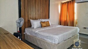 A hotel room with a bed, a wooden desk, a standing fan, and a curtain. - Room-aerol Hotel and Suites -super Suite (Lagos)