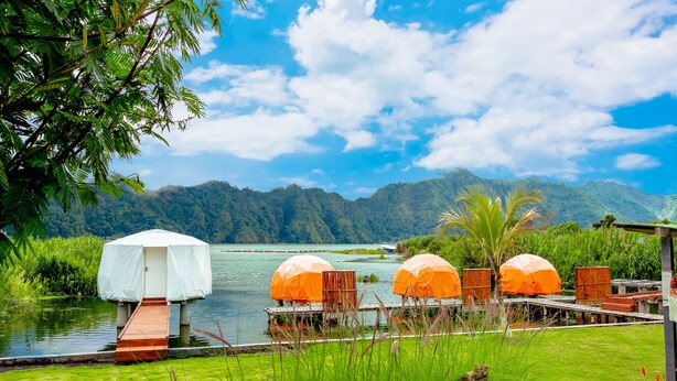 A lakeside resort with wooden deck chairs under umbrellas, a small covered structure, and lush greenery. - Jempana View (Kintamani)