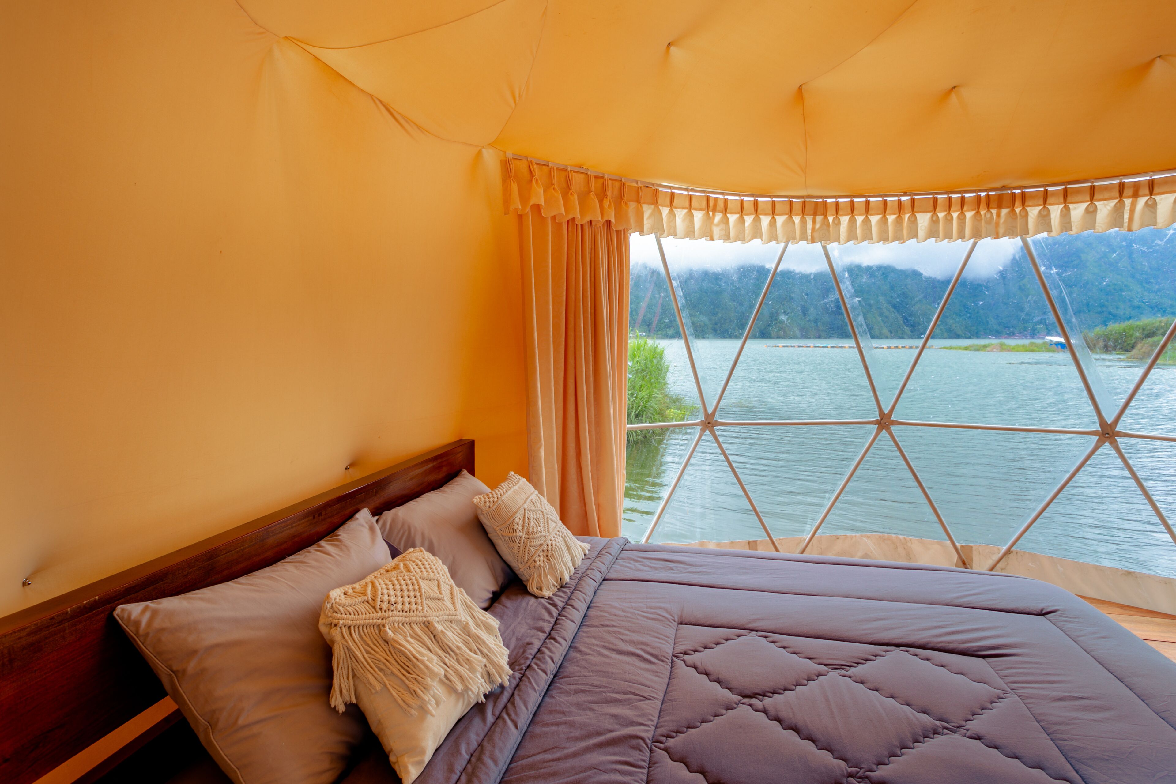 A bedroom with a large bed, a wooden headboard, and a view of a lake through a window with a geometric frame.