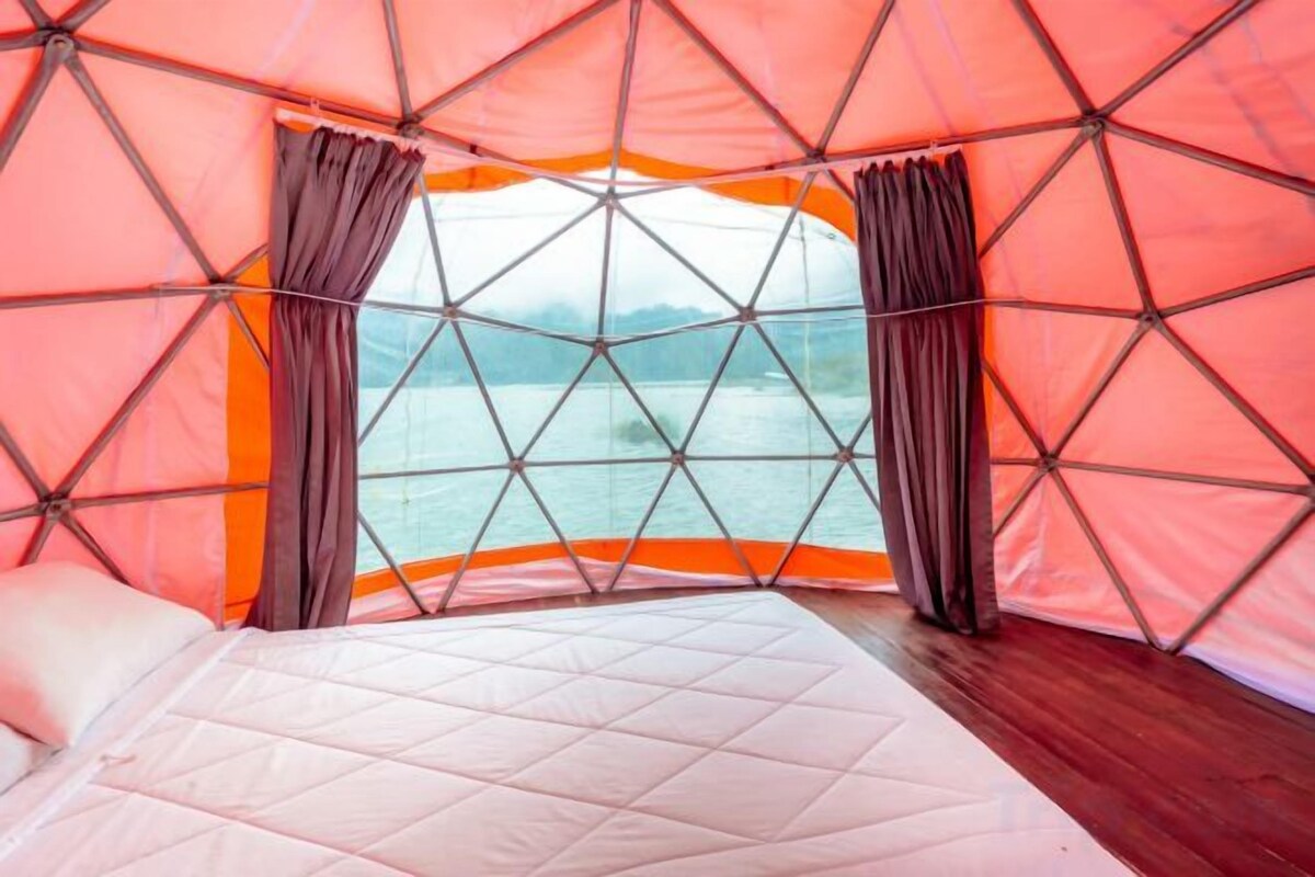 A tent with a bed inside, a view of the water, and curtains.