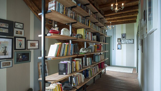 A long hallway with wooden bookshelves filled with books and various items. There are framed pictures on the walls and a chandelier hanging from the ceiling. - Room in B&B - B&b Carlonga A Double Room For Two People (Caneva)