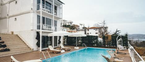 A rooftop swimming pool with lounge chairs and a white building with balconies.