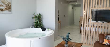 A modern living room with a large white bathtub, a wooden coffee table, a brown leather sofa, and a television on a wooden stand.