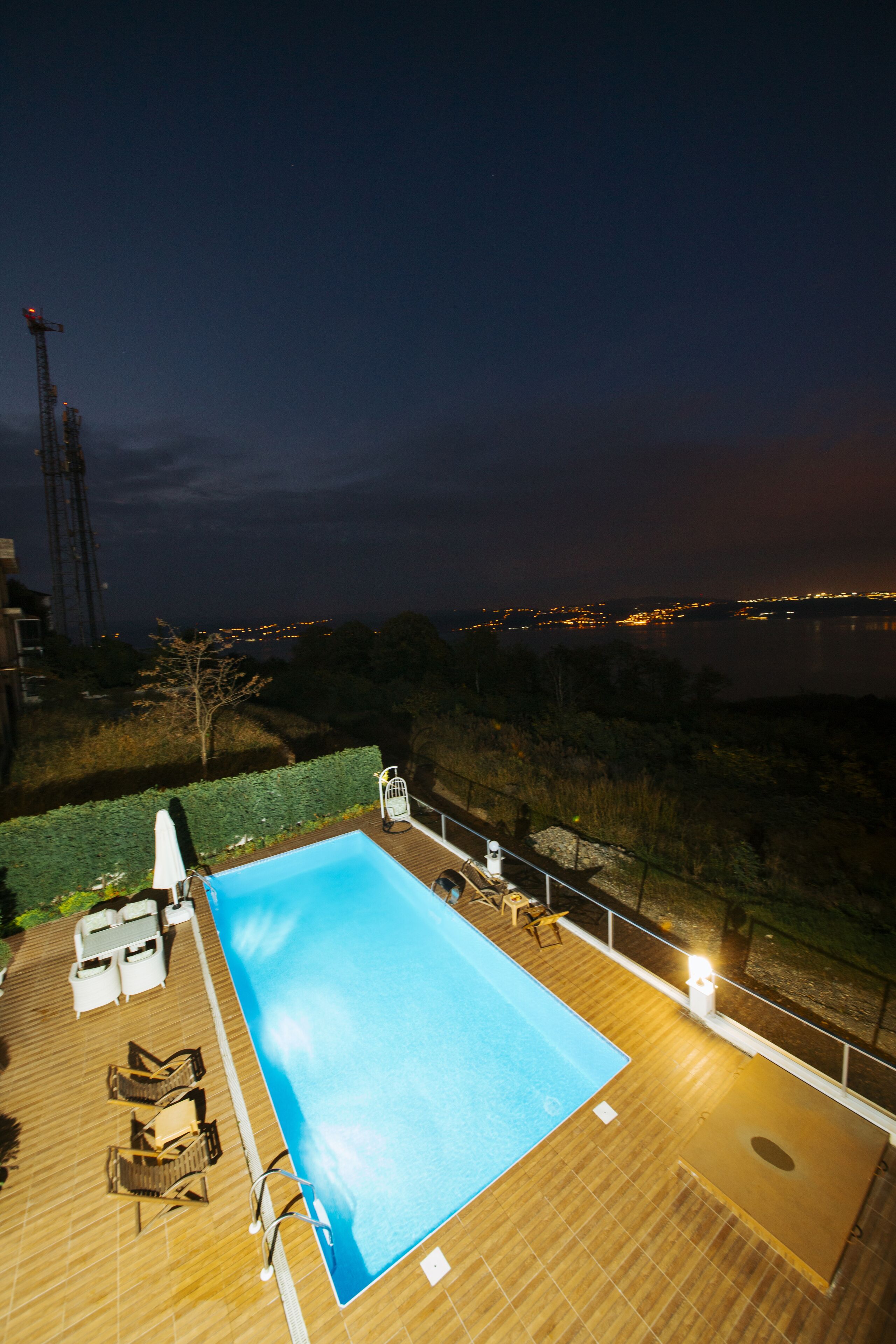 A swimming pool with lounge chairs and a wooden deck at dusk.